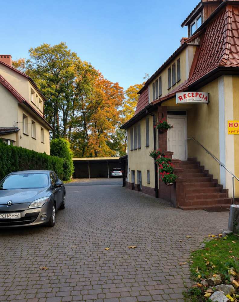 Wejście do recepcji i brukowany dziedziniec z zadaszonym parkingiem w Hotelu Pod Platanami